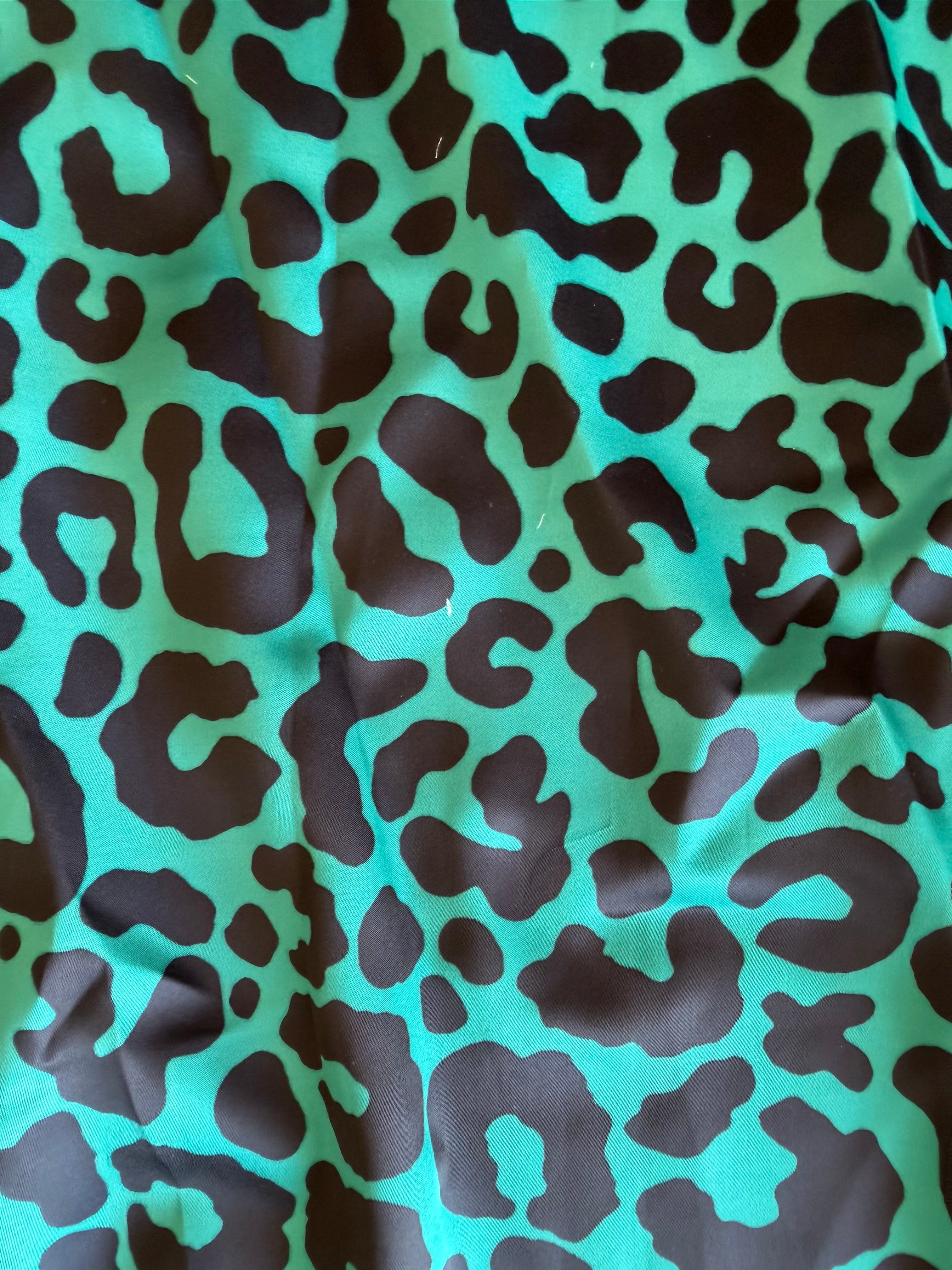 A close-up of a leopard print fabric featuring a bright turquoise green background with dark brown irregular spots