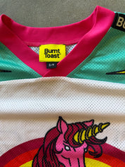 Close-up of a Burnt Toast jersey with a bright pink collar, teal mesh upper section, white mesh lower section, and a colorful unicorn graphic on the front