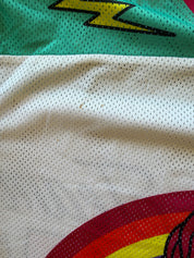 Close-up of a white mesh athletic jersey fabric with a teal top section featuring a yellow lightning bolt graphic and a red and yellow curved graphic at the bottom