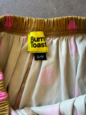 Close-up of a garment with a yellow Burn Toast label, featuring a gold elastic waistband and a cream fabric with pink polka dots