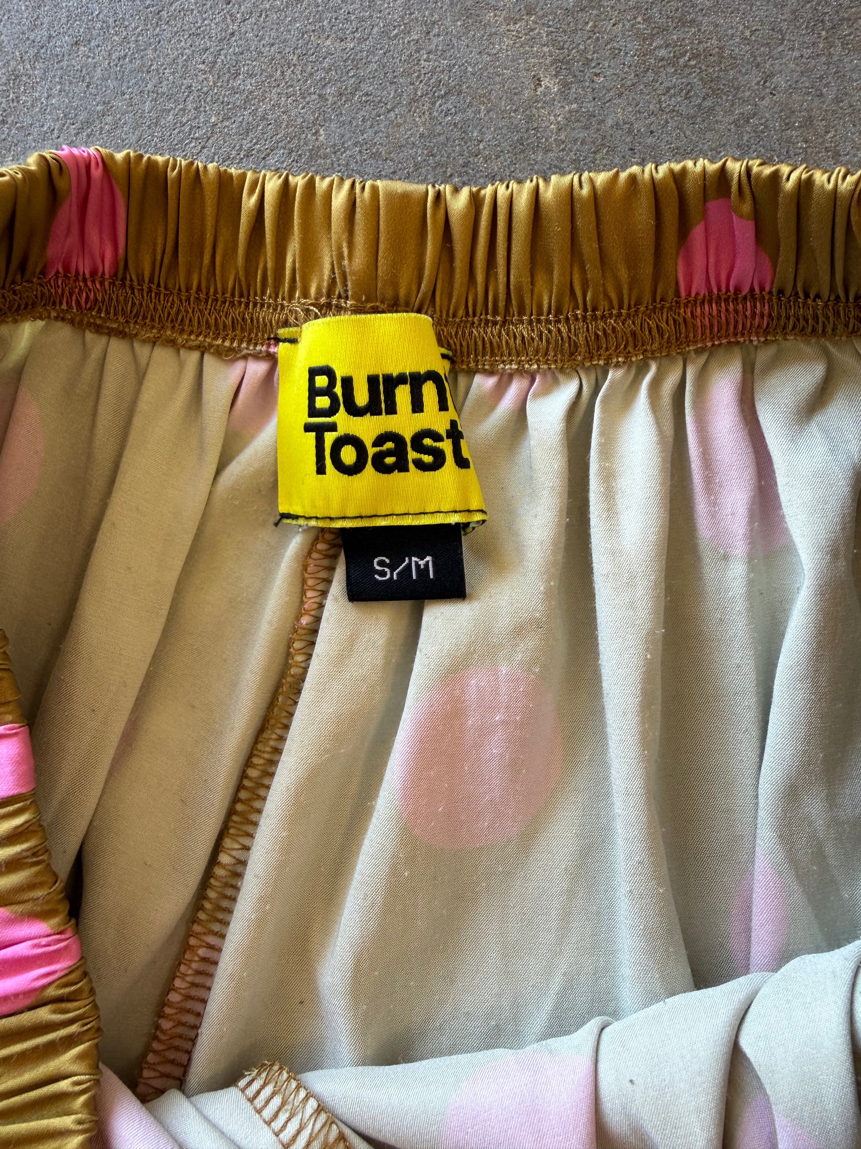Close-up of a garment with a yellow Burn Toast label, featuring a gold elastic waistband and a cream fabric with pink polka dots
