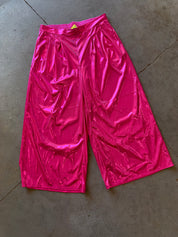 Metallic hot pink cropped pants with a shiny, crinkled texture, laid flat on a gray concrete floor