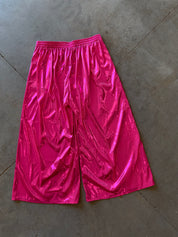 Metallic hot pink wide-leg shorts with a shiny, crinkled texture, laid flat on a gray concrete floor