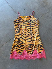 A sleeveless tiger-print camisole dress with thin pink straps and a bright pink lace hem, laid flat on a gray concrete floor