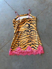A sleeveless camisole-style dress with a tiger stripe print in orange and black, featuring bright pink lace trim along the hem and matching pink straps, laid flat on a gray concrete floor