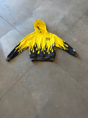 A yellow and black flame-print hoodie with 'Burnt Toast' printed on the chest, laid flat on a gray concrete floor