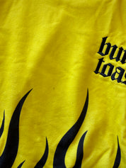 Close-up of a bright yellow fabric surface with black flame graphics and partial black gothic text reading 'burn toast'