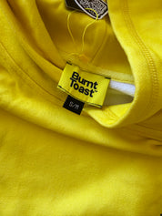 Close-up of a bright yellow garment showing the inner neck area, with a visible Burnt Toast brand label and a small black size tag marked S/M