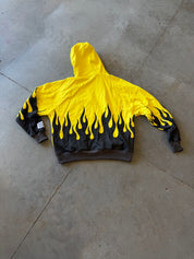 A yellow hooded sweatshirt with a black flame print along the bottom hem and cuffs, laid flat on a gray concrete floor