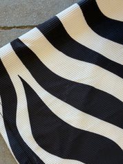 A close-up of a black and off-white wavy striped fabric, showing a ribbed texture, laid on a gray concrete surface