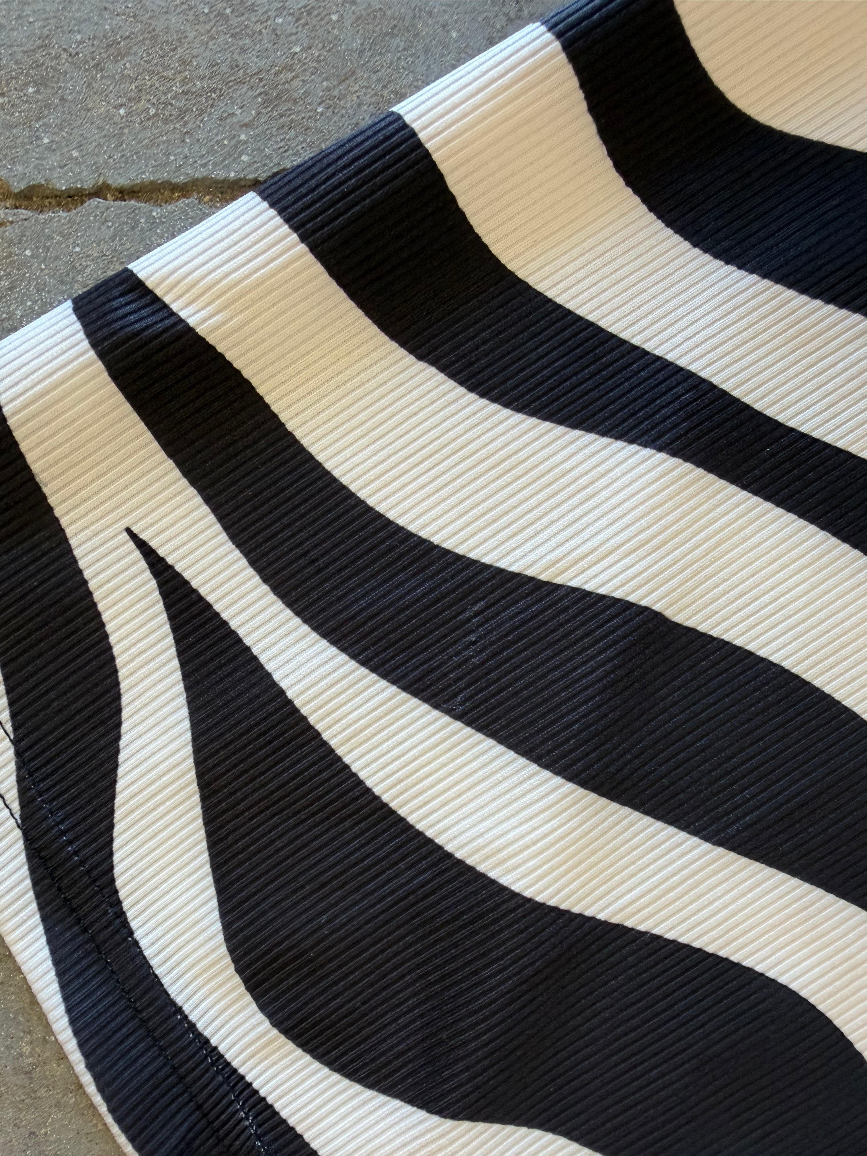 A close-up of a black and off-white wavy striped fabric, showing a ribbed texture, laid on a gray concrete surface