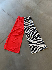 Two pairs of wide-leg athletic shorts laid flat on a concrete floor: one solid bright red and one black and white zebra print