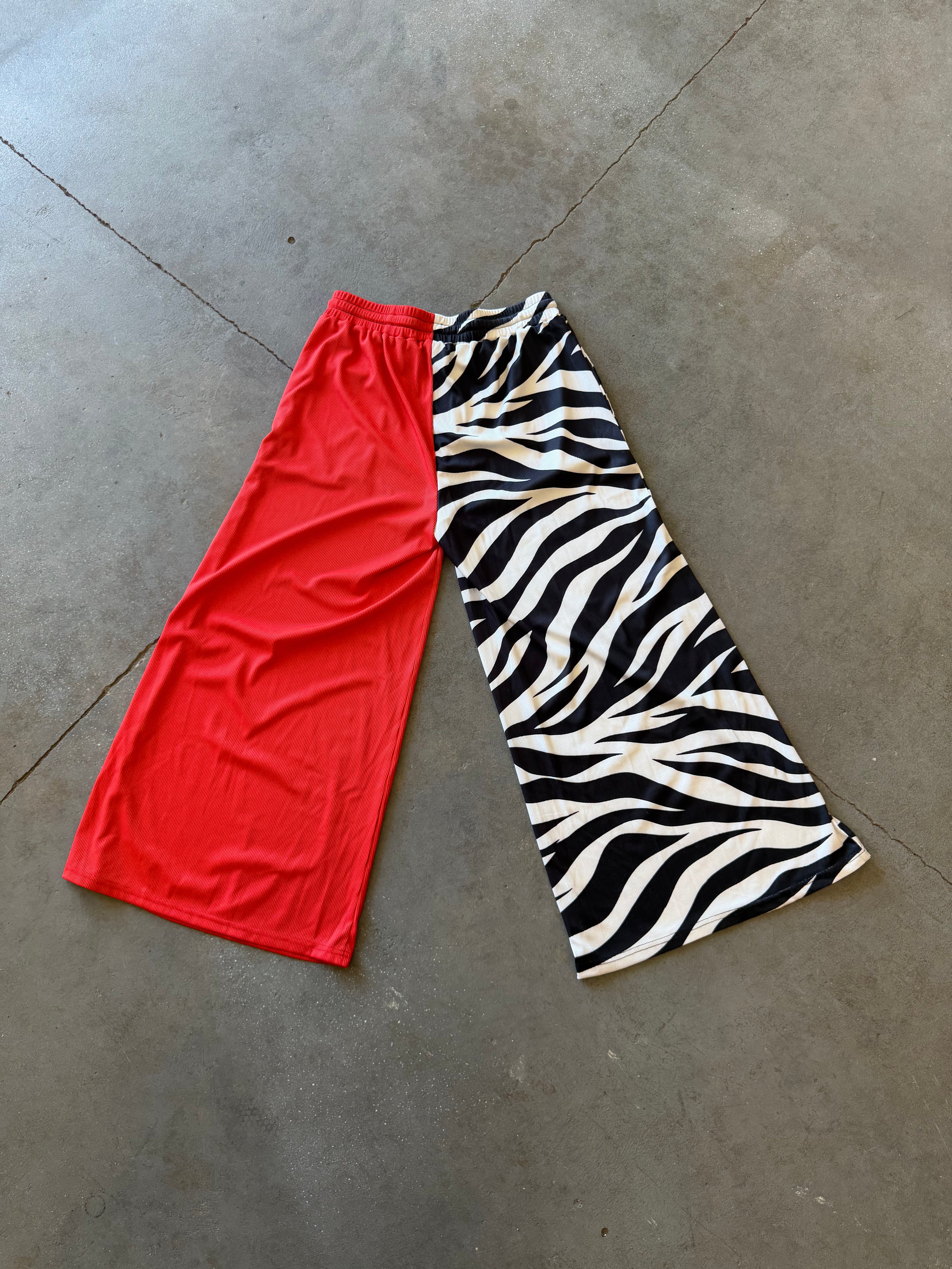 Two pairs of wide-leg athletic shorts laid flat on a concrete floor: one solid bright red and one black and white zebra print