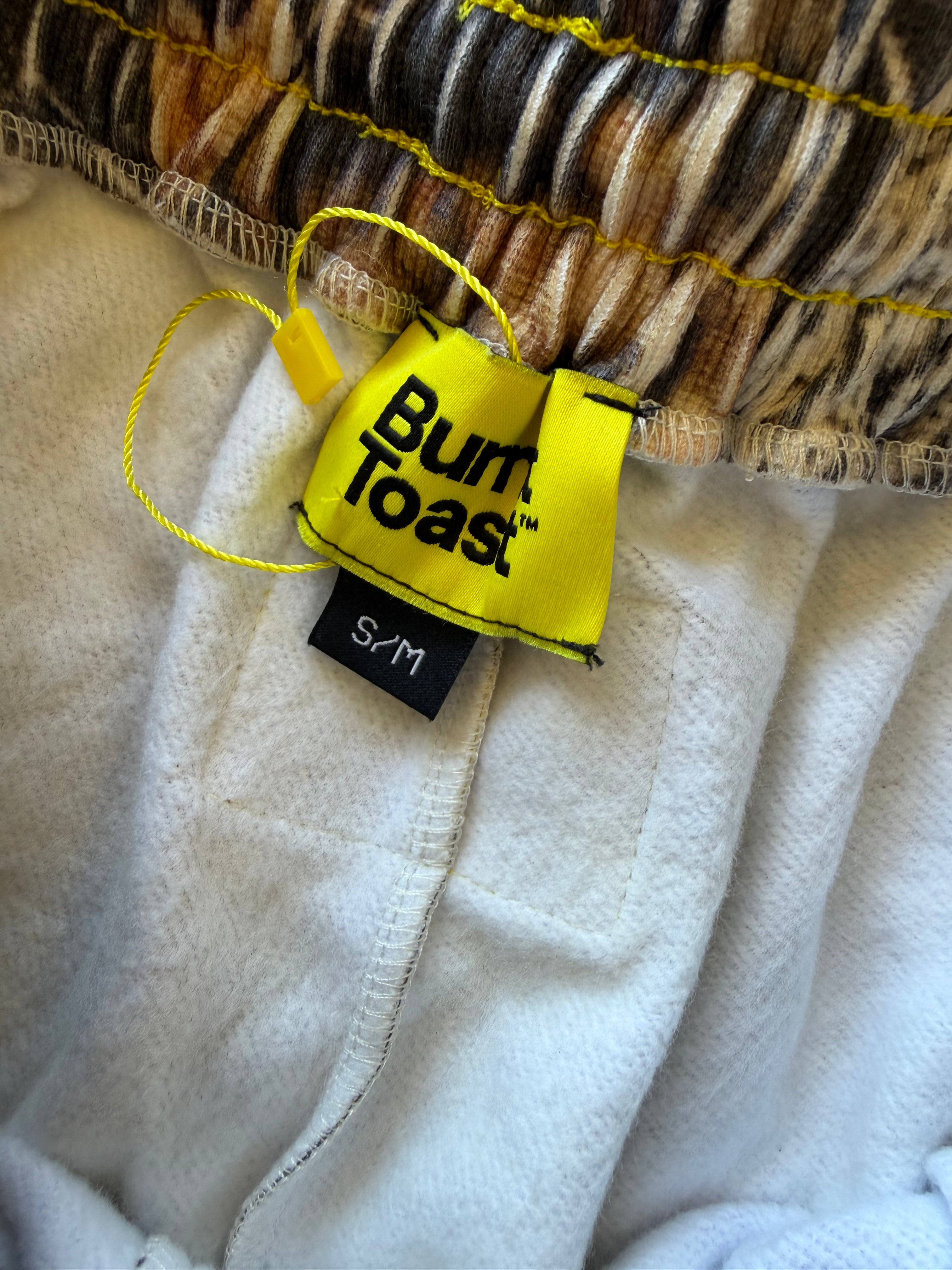 Close-up of a white fleece garment with a yellow Burn Toast brand tag and a brown-and-black patterned fabric at the top.