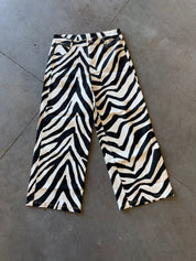 Black and beige zebra-print cropped pants laid flat on a gray concrete floor