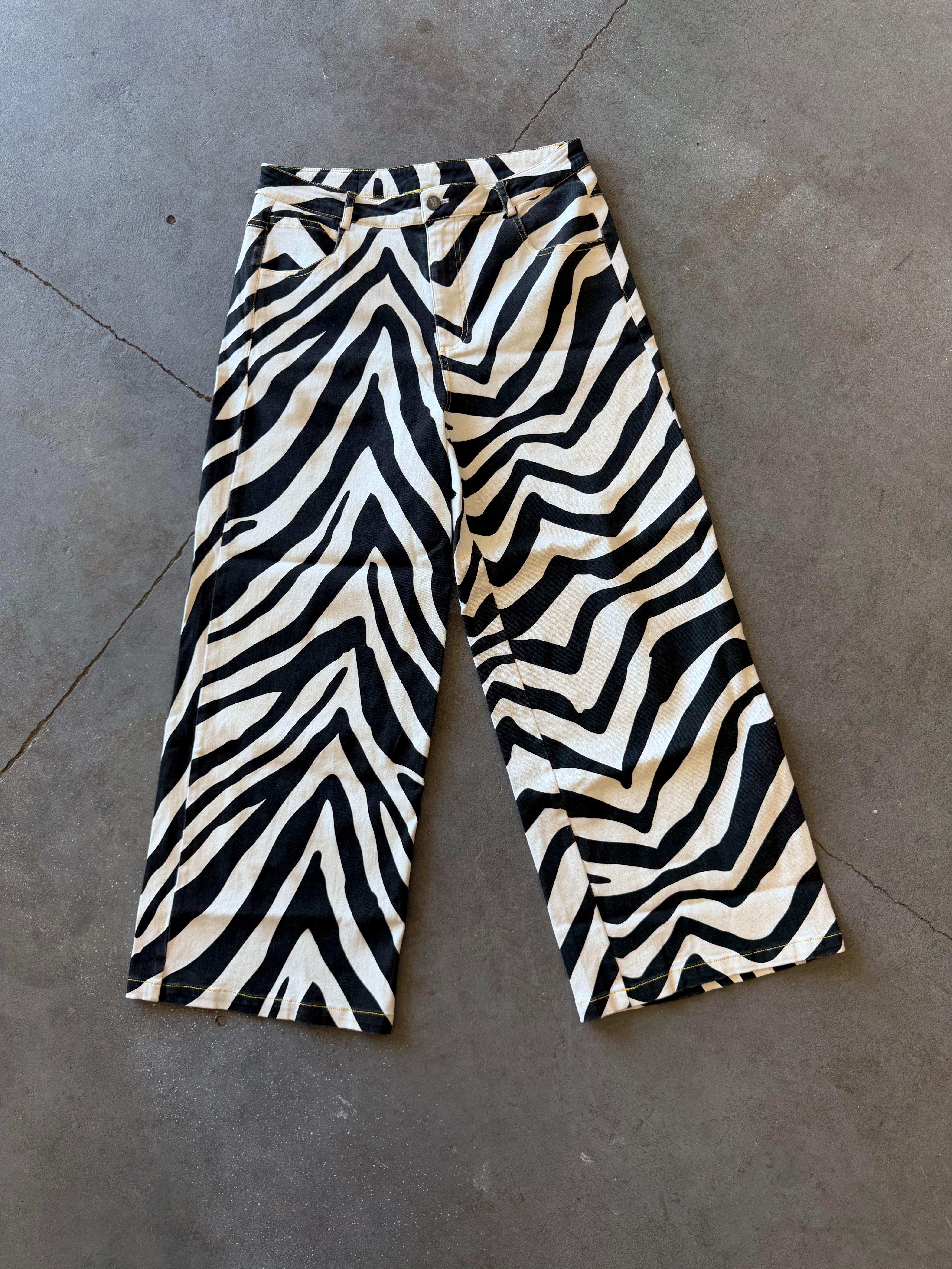 Black and beige zebra-print cropped pants laid flat on a gray concrete floor
