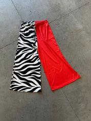 A pair of wide-leg cropped pants laid flat on a gray concrete floor, featuring a split design with a black and white zebra print on one side and a solid bright red on the other