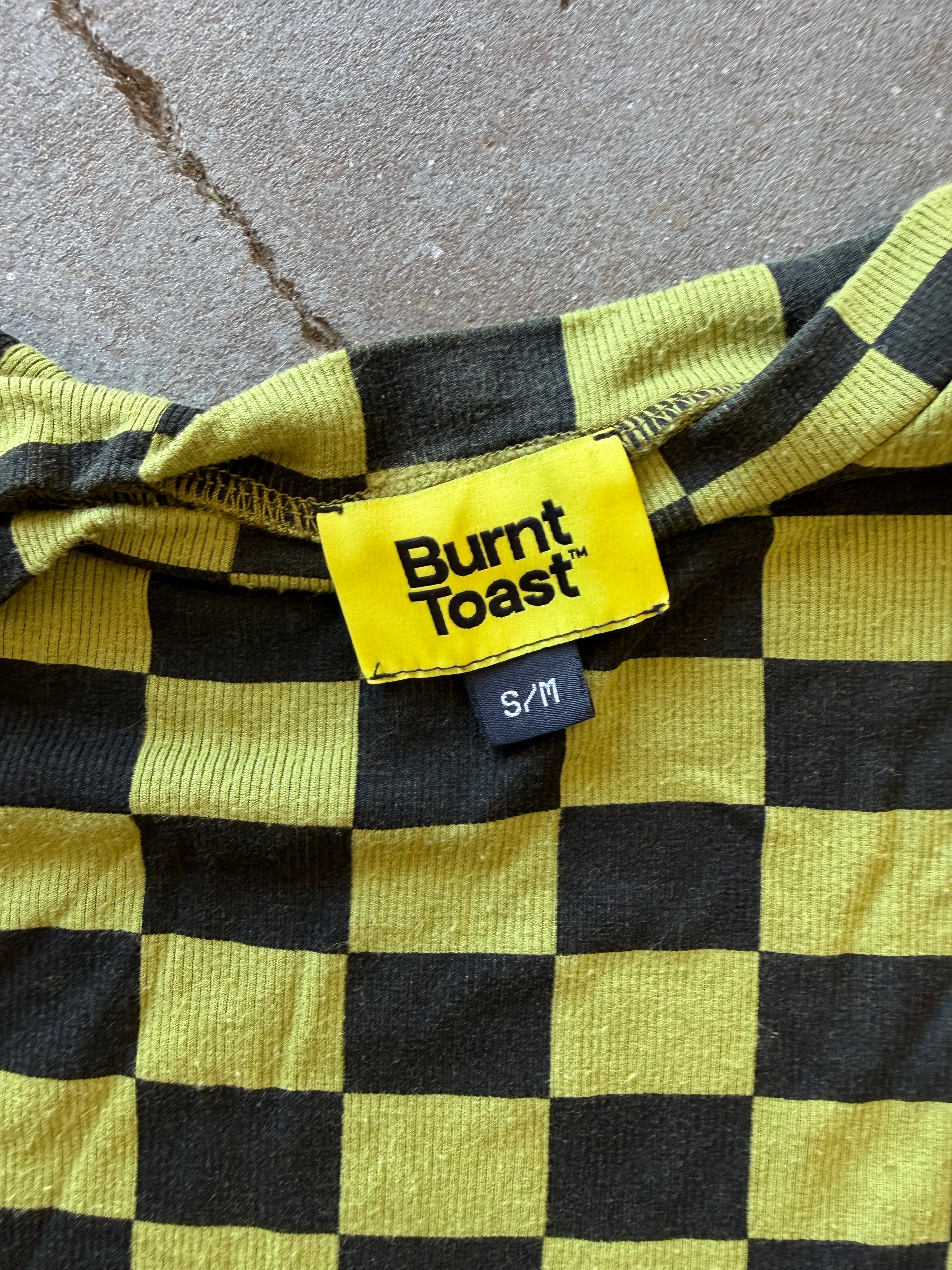 Close-up of a yellow and black checkered garment with a visible Burnt Toast brand label and size S/M, laid flat on a gray concrete surface