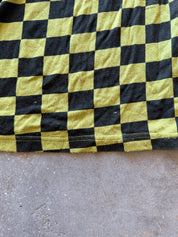 A close-up of a black and yellow checkerboard patterned fabric, likely a sweatshirt or blanket, laid flat on a gray concrete floor