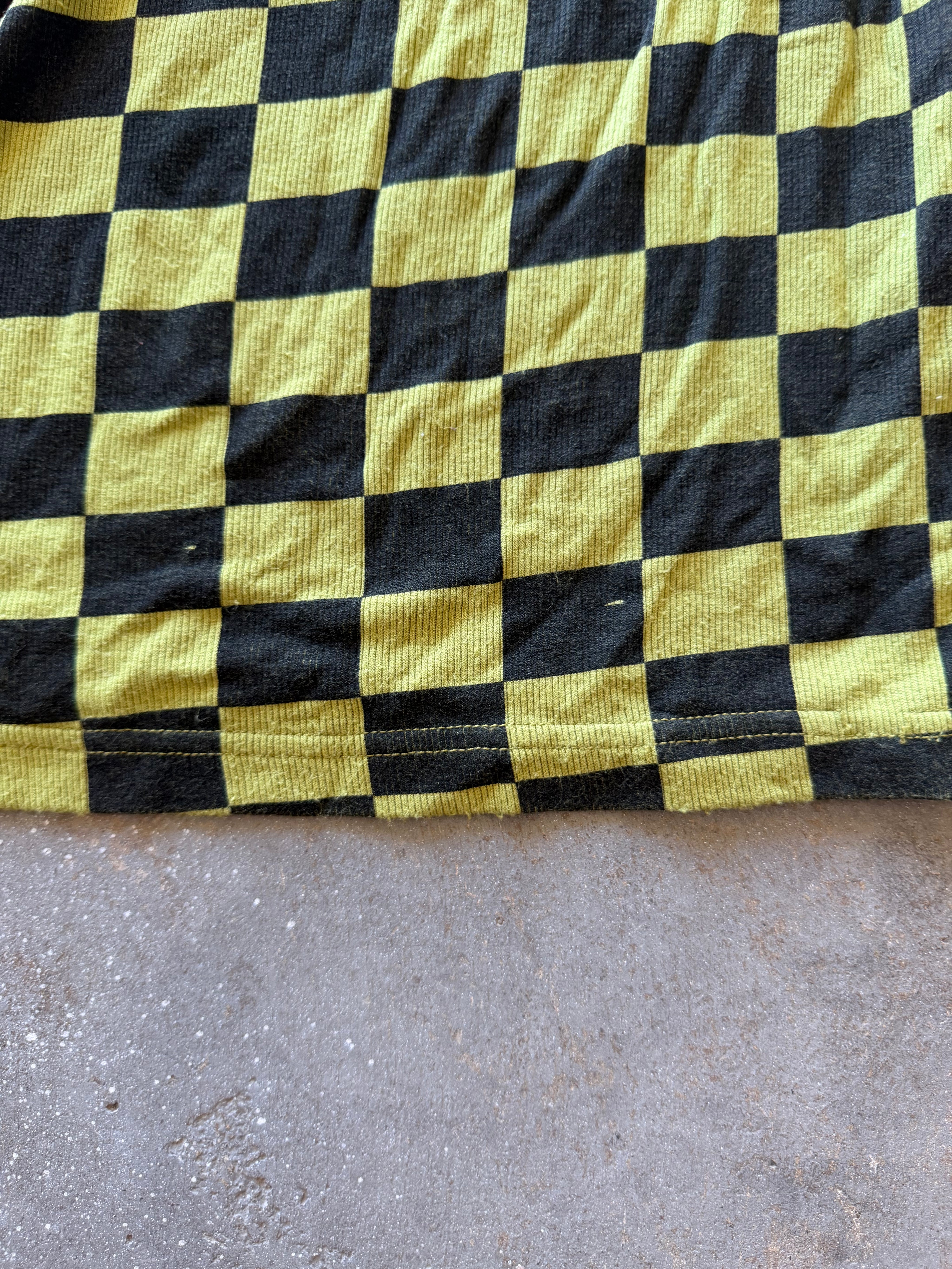 A close-up of a black and yellow checkerboard patterned fabric, likely a sweatshirt or blanket, laid flat on a gray concrete floor