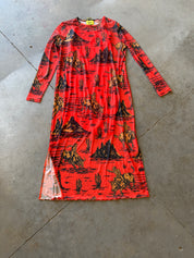 A long-sleeve red dress with a black and orange western-style print of mountains, cacti, and riders, laid flat on a gray concrete floor