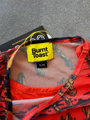 Close-up of a Burnt Toast garment with a bright yellow brand label, showing a red and black patterned fabric with sheer mesh