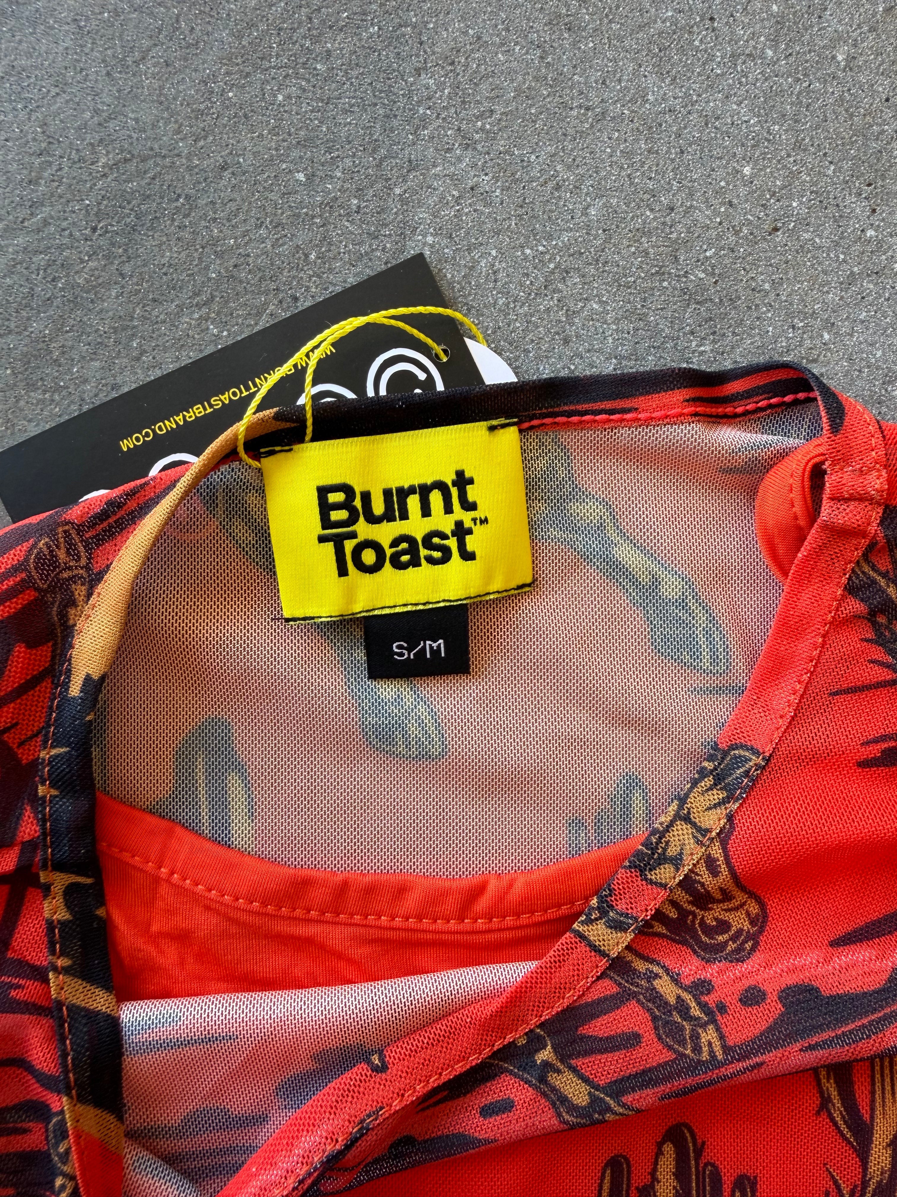 Close-up of a Burnt Toast garment with a bright yellow brand label, showing a red and black patterned fabric with sheer mesh