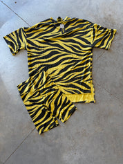 A two-piece matching set consisting of a short-sleeve t-shirt and shorts, both featuring a bold green and black zebra stripe pattern, laid flat on a gray concrete floor