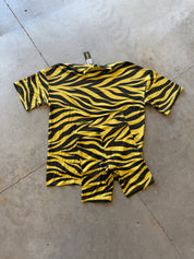 A short-sleeve baby t-shirt and matching shorts set in a yellow and black zebra print, laid flat on a gray concrete floor