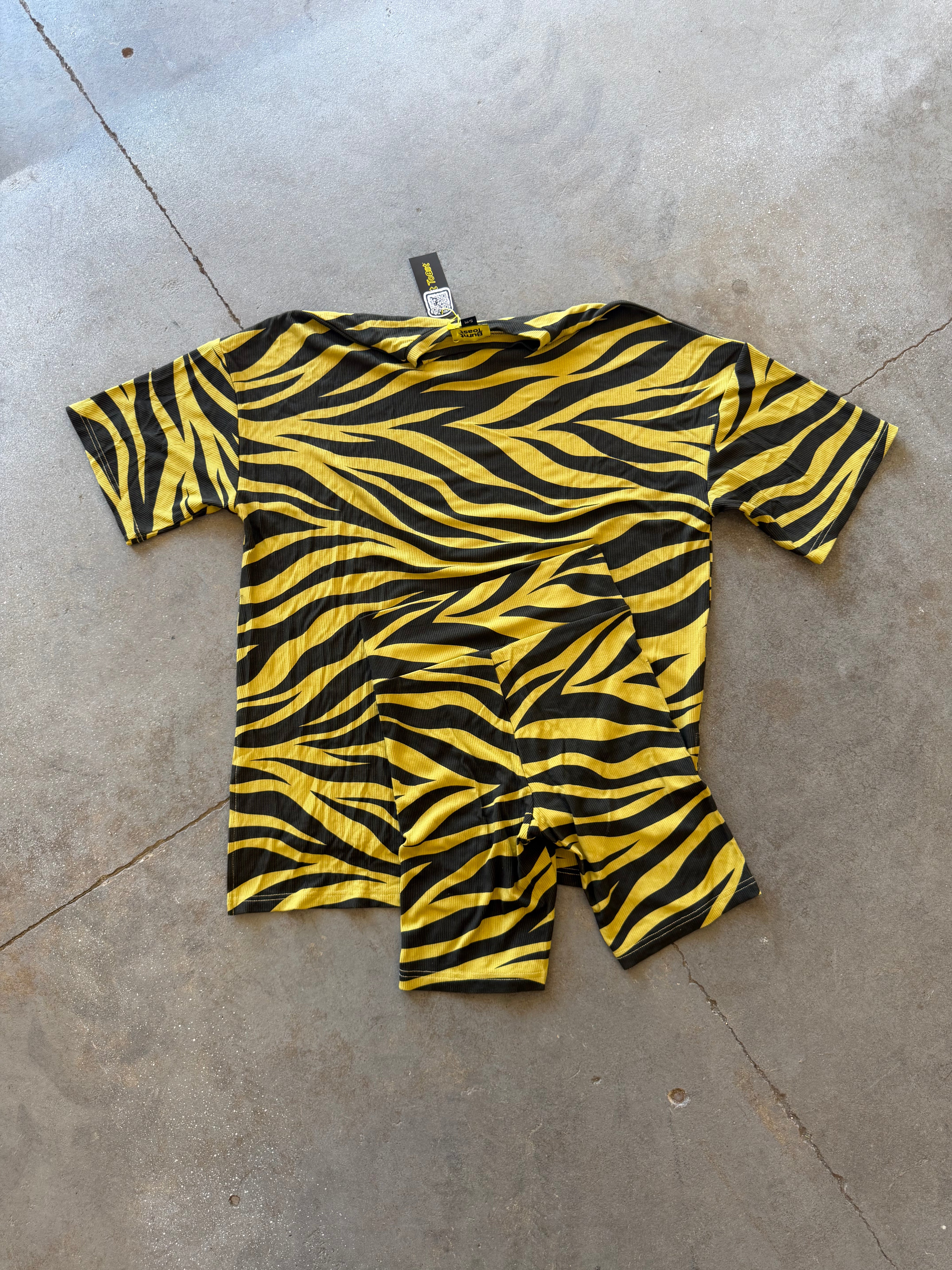 A short-sleeve baby t-shirt and matching shorts set in a yellow and black zebra print, laid flat on a gray concrete floor