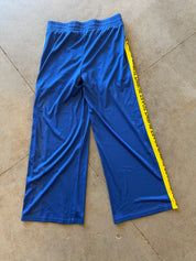 Blue athletic cropped pants with a yellow side stripe featuring black text, laid flat on a concrete floor