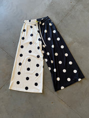 A pair of wide-leg cropped pants laid flat on a concrete floor, featuring a split design with one half in cream with black polka dots and the other half in black with white polka dots