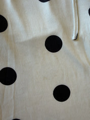 A close-up of a ribbed fabric with a black polka dot pattern on an off-white background