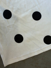 A close-up of a white ribbed fabric item, likely a towel or blanket, featuring four black polka dots arranged in a square pattern, laid on a gray concrete floor