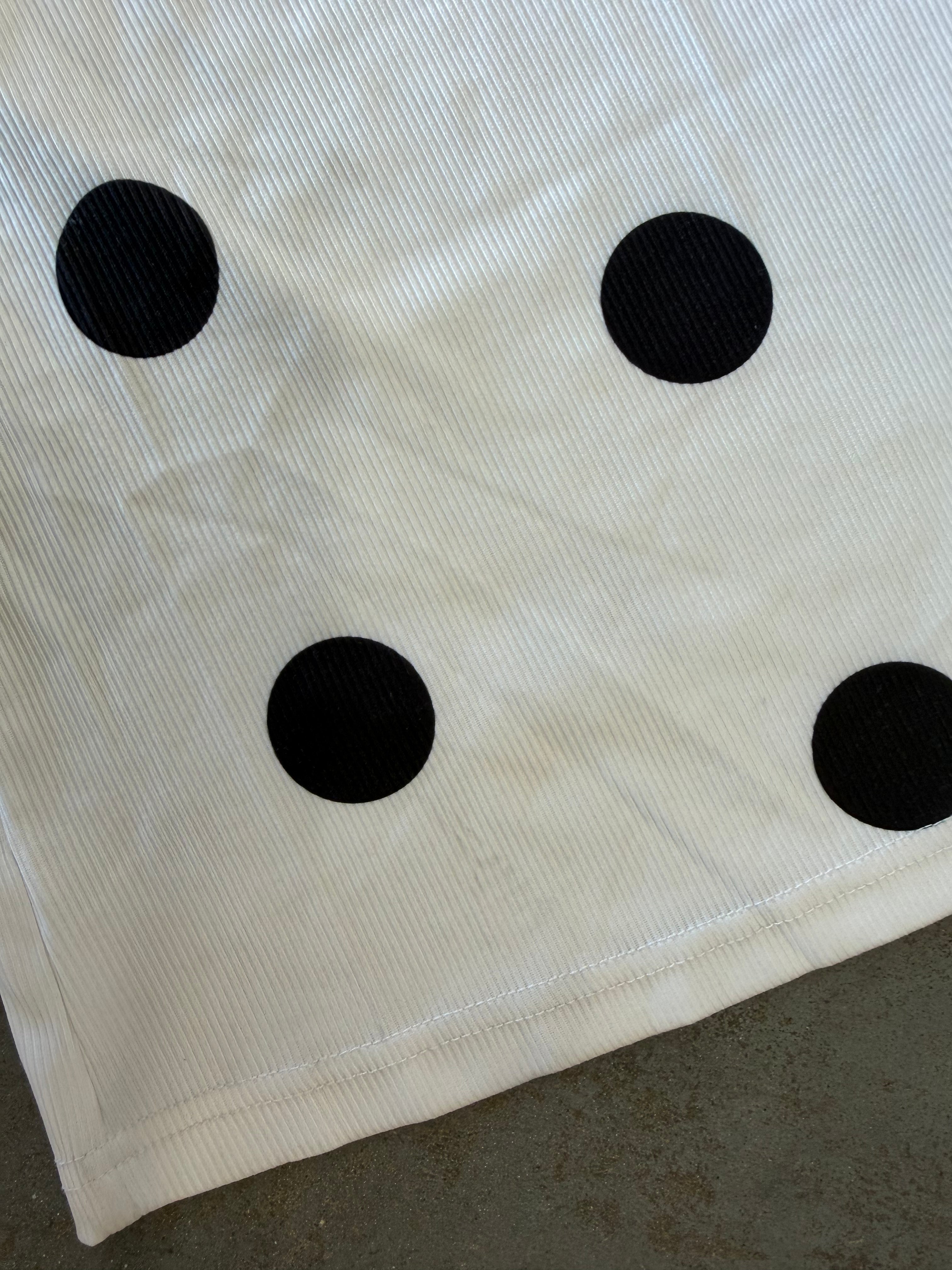 A close-up of a white ribbed fabric item, likely a towel or blanket, featuring four black polka dots arranged in a square pattern, laid on a gray concrete floor