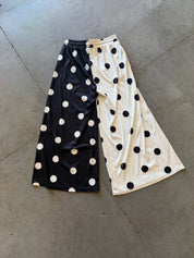 A pair of wide-leg cropped pants laid flat on a gray concrete floor, featuring a split design with one leg in black and white polka dots and the other in cream and black polka dots