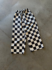 Black and white checkerboard cropped pants laid flat on a gray concrete floor