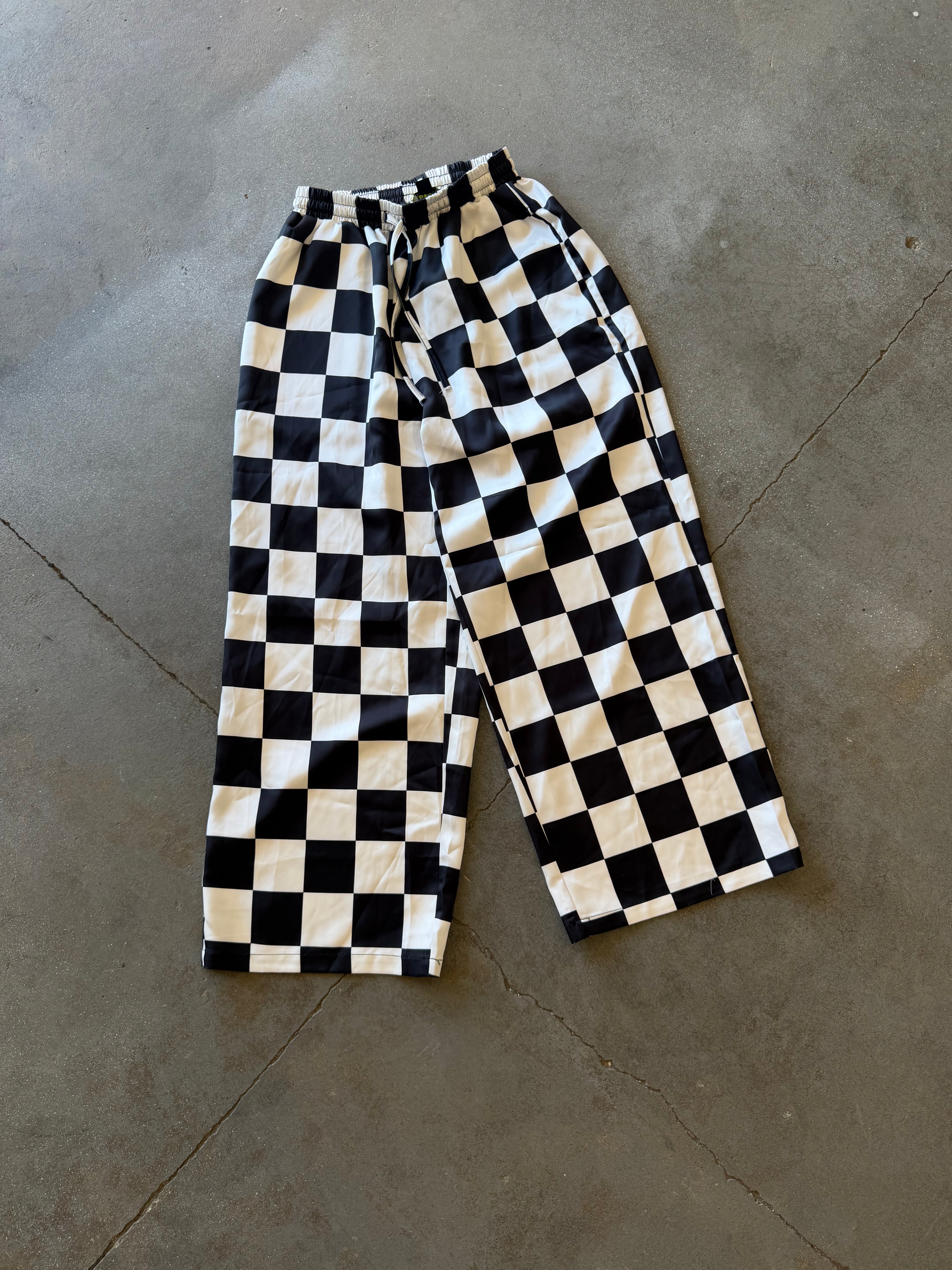 Black and white checkerboard cropped pants laid flat on a gray concrete floor