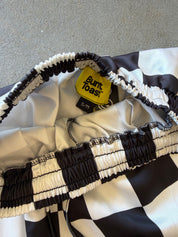 Close-up of a black and white checkered garment with gathered elastic trim and a yellow Buntast tag reading S/M