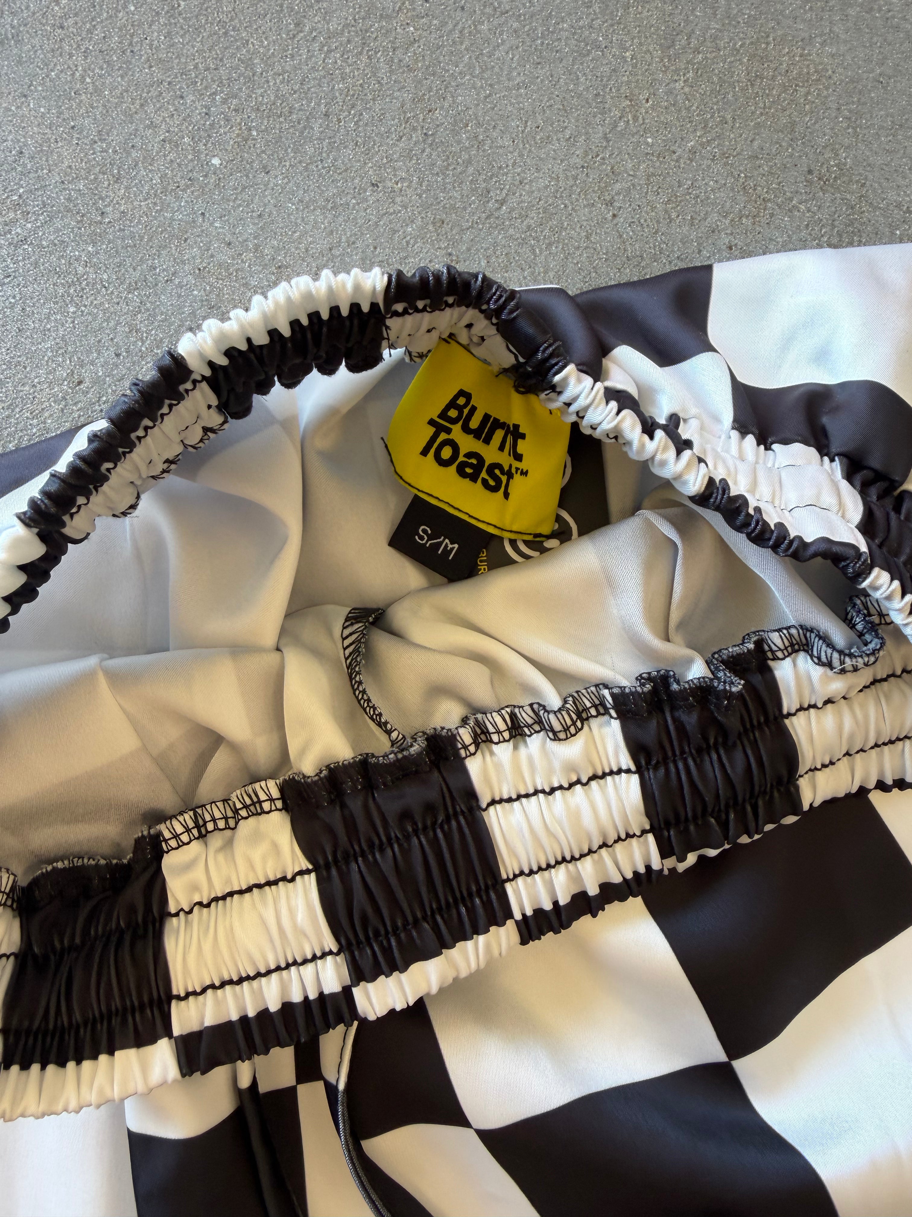 Close-up of a black and white checkered garment with gathered elastic trim and a yellow Buntast tag reading S/M