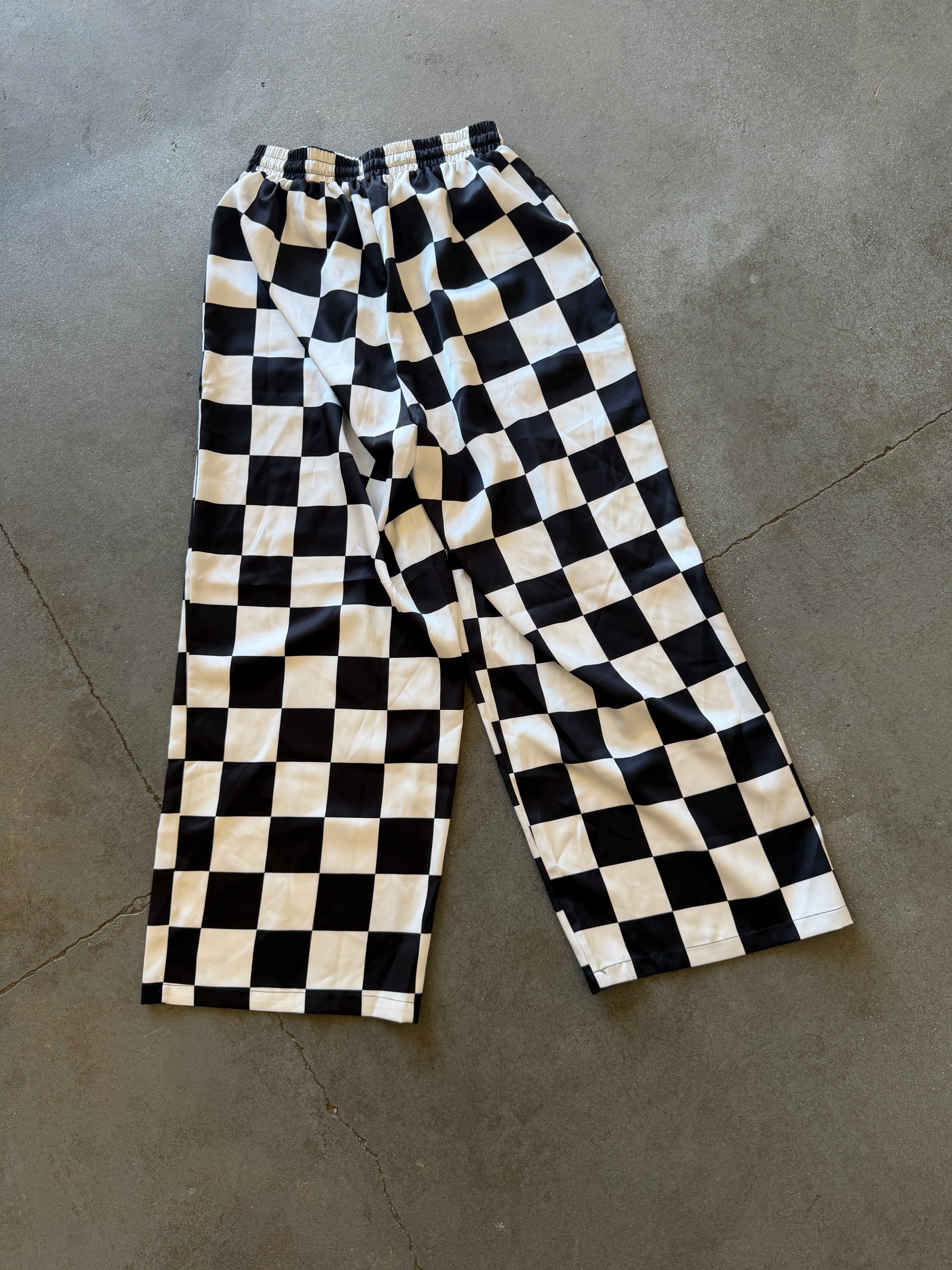 Black and cream checkerboard cropped pants laid flat on a gray concrete floor