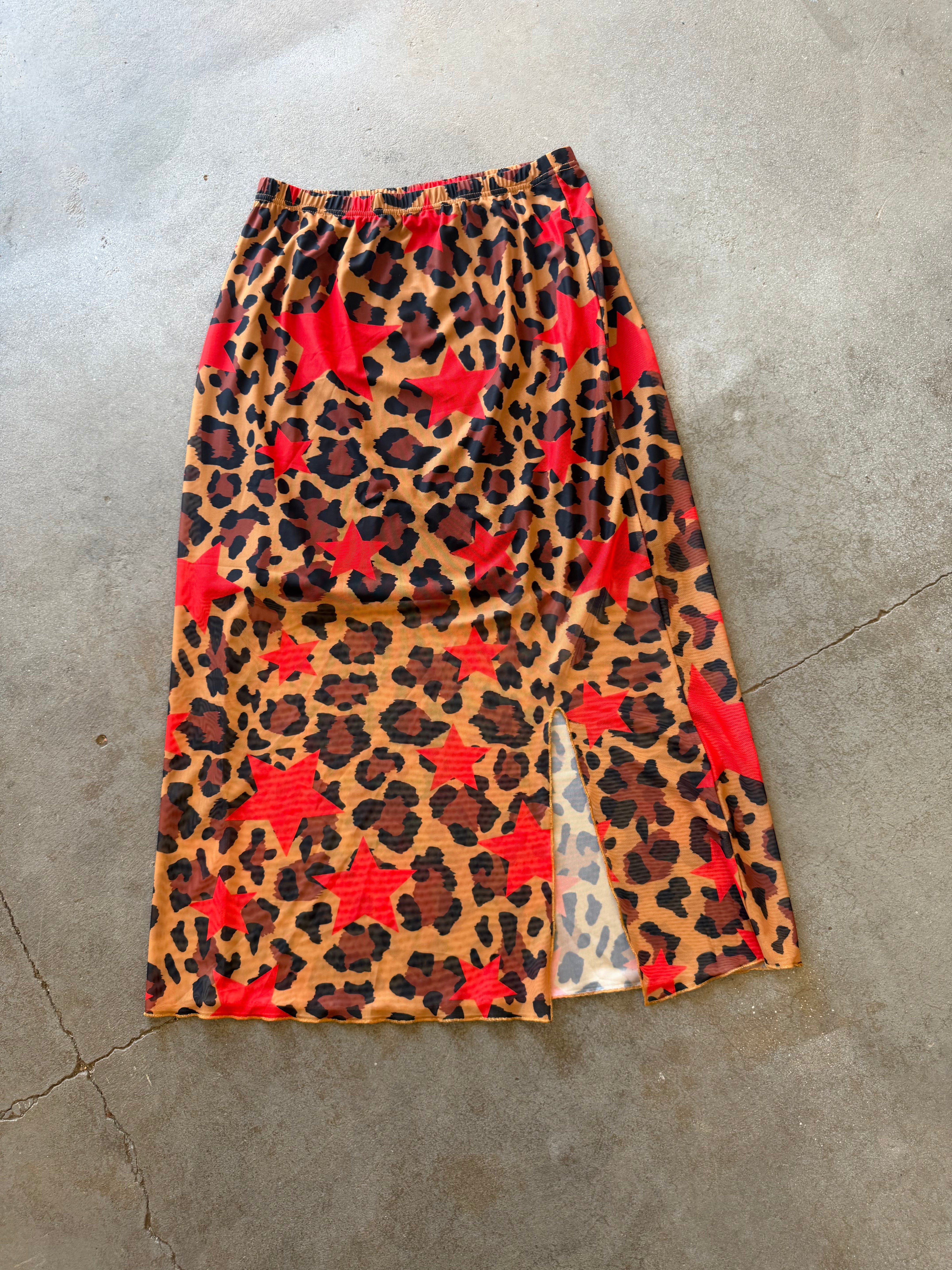 A leopard print midi skirt with red star patterns, laid flat on a gray concrete floor