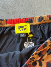 Close-up of the waistband and inner label of Burnt Toast shorts, showing a yellow brand label, black inner lining, and a multicolor leopard print pattern in orange, black, and brown