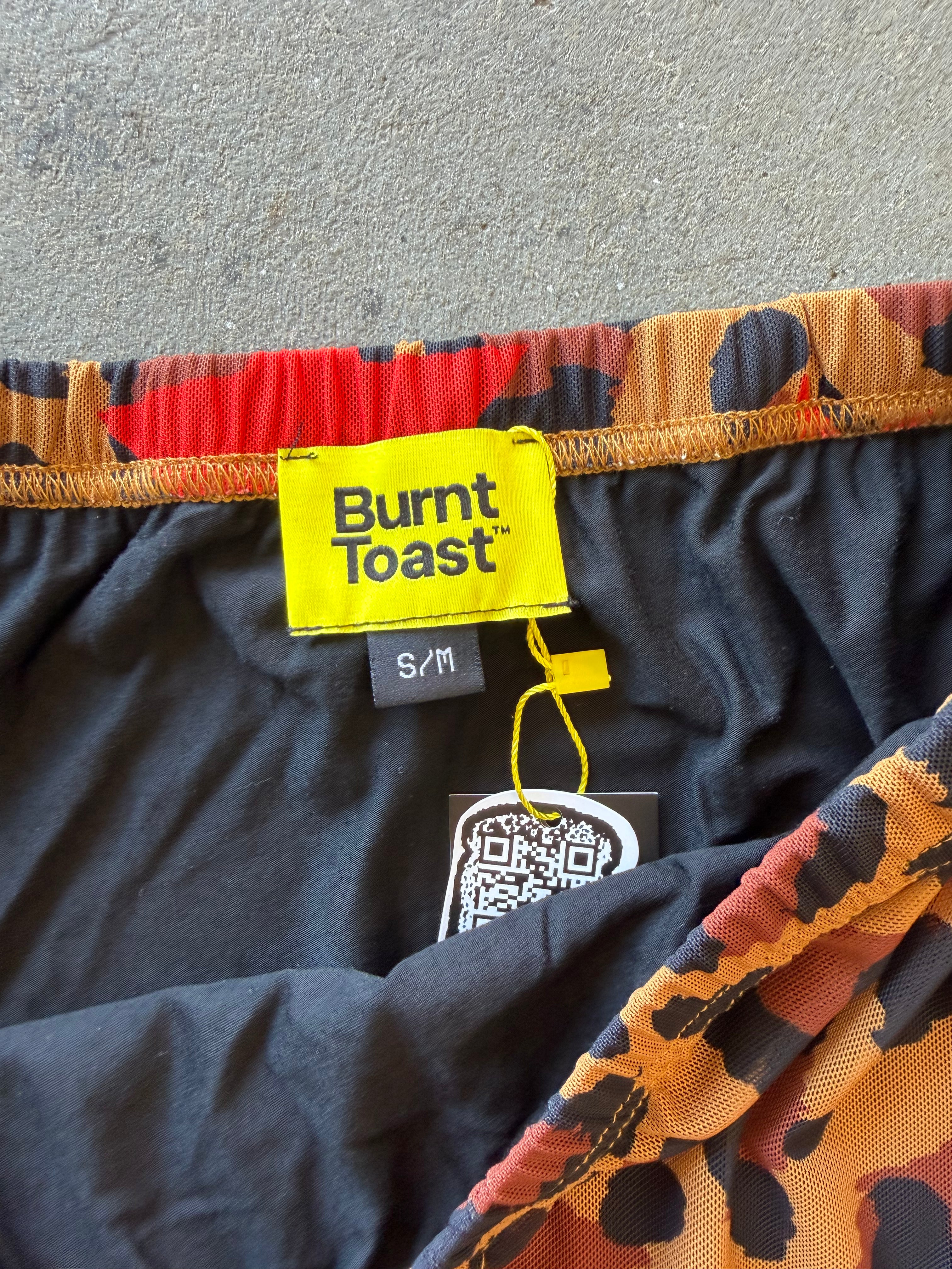 Close-up of the waistband and inner label of Burnt Toast shorts, showing a yellow brand label, black inner lining, and a multicolor leopard print pattern in orange, black, and brown