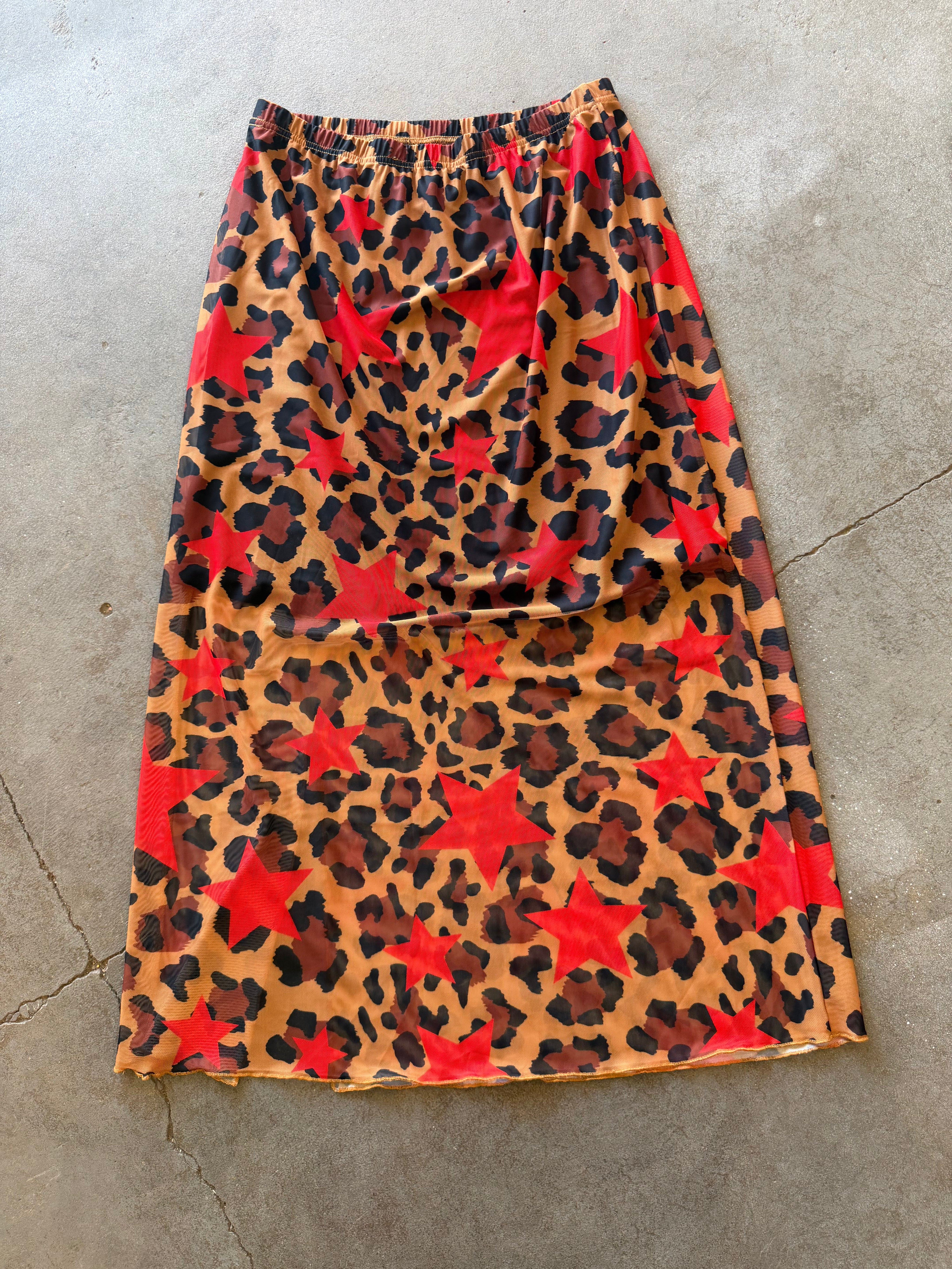 A leopard-print skirt with red star motifs, laid flat on a gray concrete floor