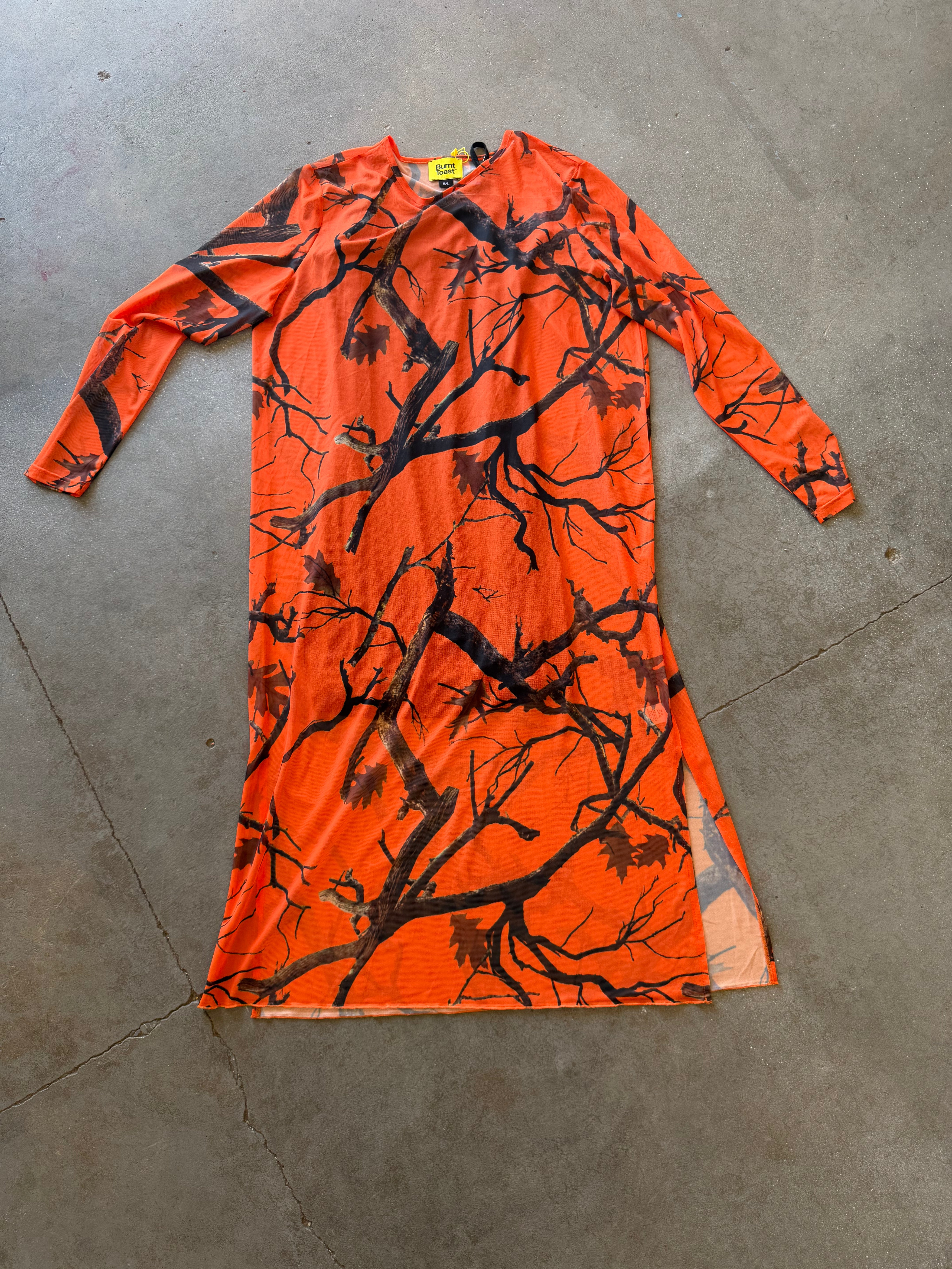 An orange long-sleeve dress with a black tree branch camouflage pattern, laid flat on a gray concrete floor