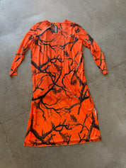 An orange long-sleeve dress with a black tree branch and leaf pattern, laid flat on a gray concrete floor