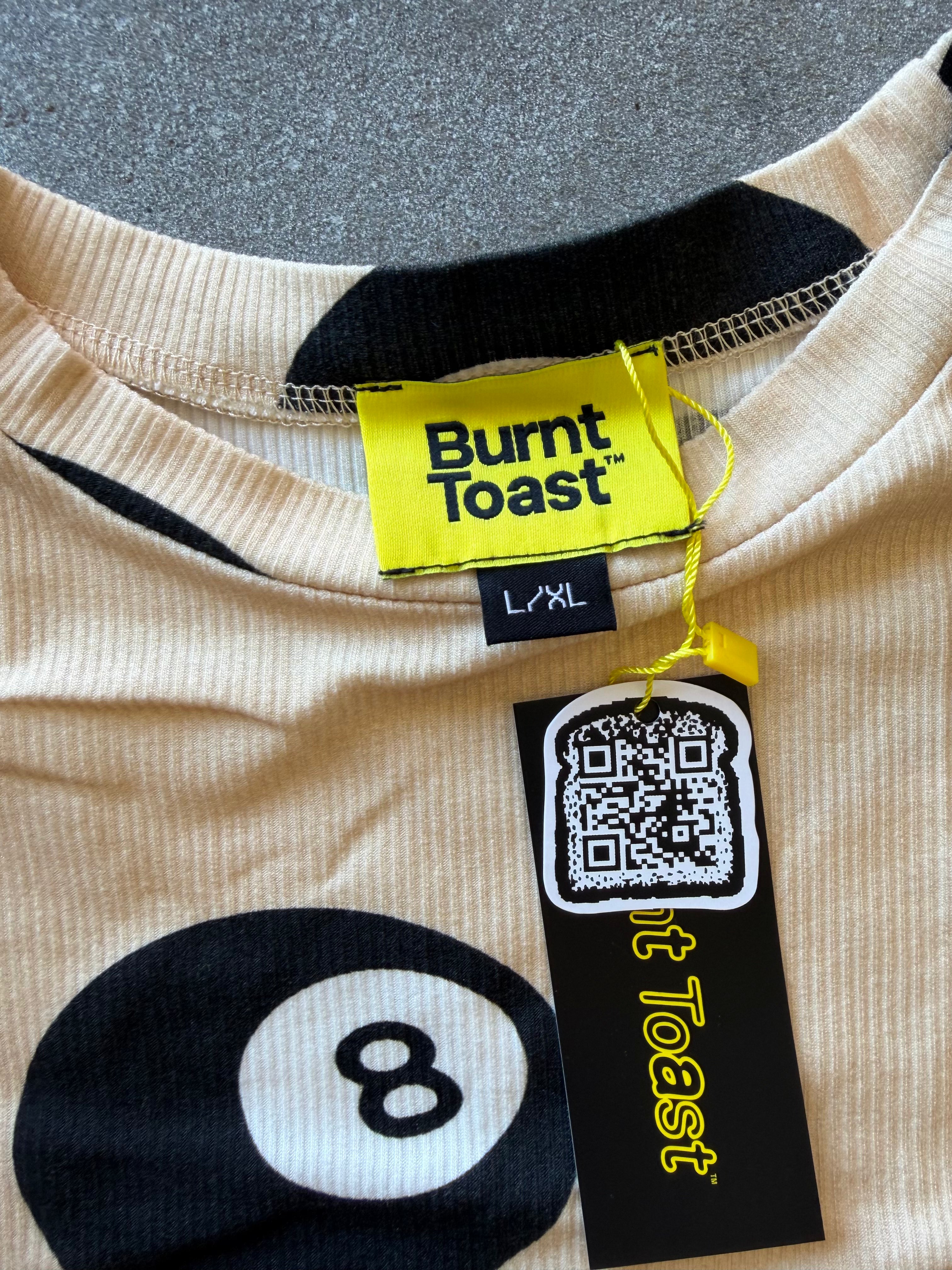Close-up of a beige ribbed knit top with black graphic print, featuring a large billiard 8-ball motif and a yellow Burnt Toast brand tag with a QR code hangtag