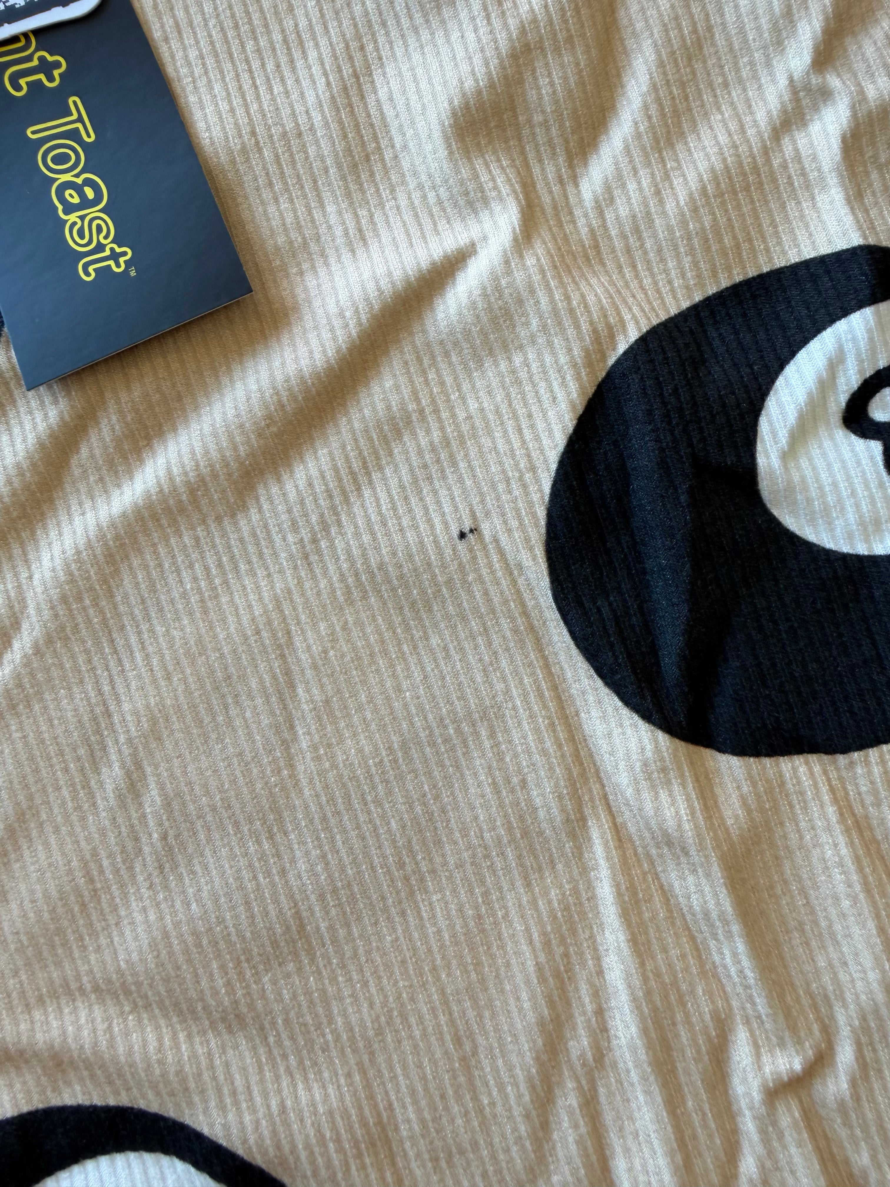 A close-up of a beige ribbed knit garment with a large black-and-white 8-ball graphic and a visible black hangtag reading 'Burnt Toast'