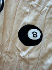 Close-up of a beige ribbed fabric garment featuring a black and white 8-ball pool icon printed on the front
